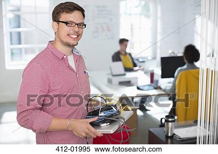 Businessman carrying cords and laptop in office View Large Photo Image Stock Photography - Businessman carrying cords and laptop in office. Fotosearch