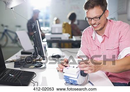 Stock Image - Businessman looking up address in office. Fotosearch