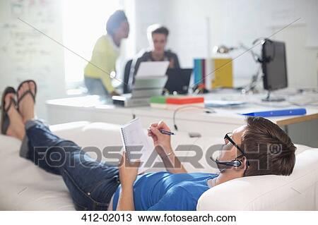 Businessman taking notes on sofa in office View Large Photo Image Stock Image - Businessman taking notes on sofa in office. Fotosearch