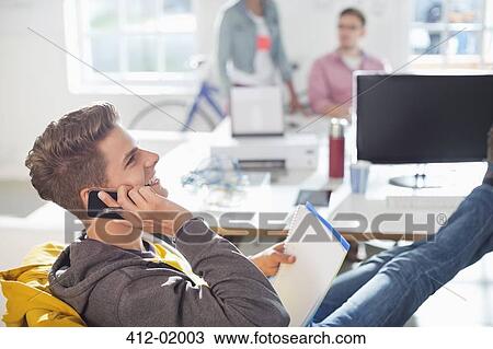Stock Image - Businessman talking on cell phone in office. Fotosearch