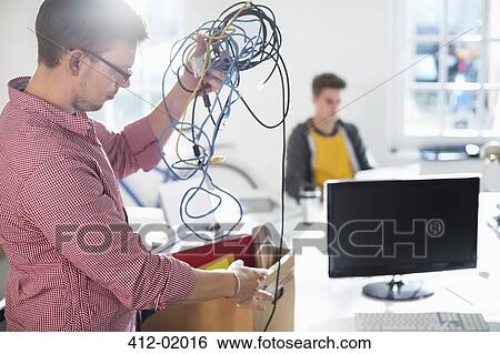 Businessman untangling cords in office View Large Photo Image Stock Photograph - Businessman untangling cords in office. Fotosearch