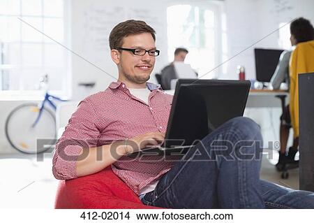 Picture - Businessman using laptop in bean bag chair in office. Fotosearch