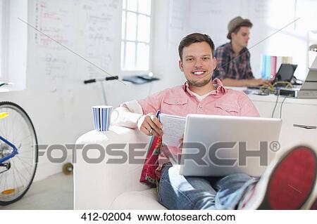 Picture - Businessman using laptop on sofa in office. Fotosearch