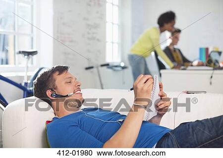 Man in headset taking notes on sofa View Large Photo Image Stock Image - Man in headset taking notes on sofa. Fotosearch
