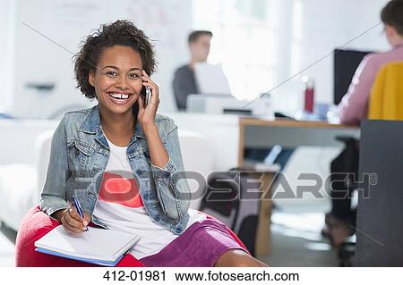 Stock Image - Woman taking notes on cell phone in office. Fotosearch
