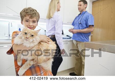 Stock Photo - Owner holding cat in vet's surgery. Fotosearch