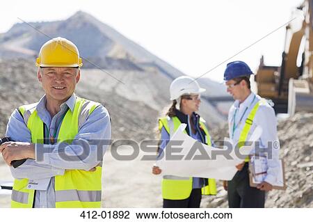 Businessman in hard hat smiling in quarry View Large Photo Image Stock Image - Businessman in hard hat smiling in quarry. Fotosearch