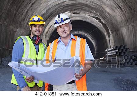 Stock Image - Workers reading blueprints in tunnel. Fotosearch