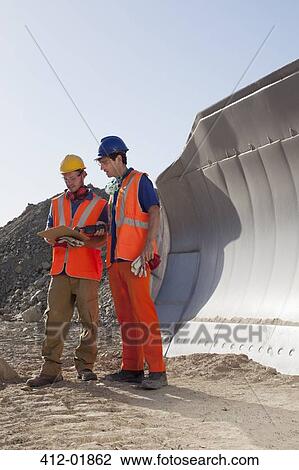 Stock Image - Workers talking by machinery in quarry. Fotosearch