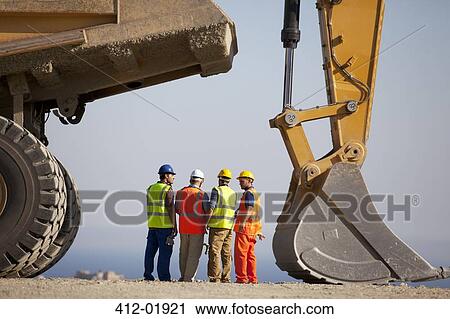 Stock Image - Workers talking by machinery in quarry. Fotosearch