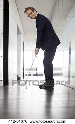 Businessman putting golf ball in office View Large Photo Image Stock Image - Businessman putting golf ball in office. Fotosearch