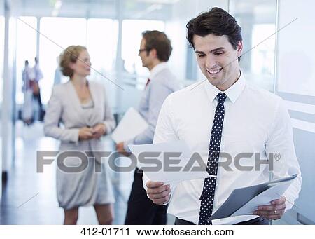 Businessman reading papers in office hallway View Large Photo Image Stock Image - Businessman reading papers in office hallway. Fotosearch