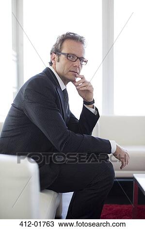 Businessman sitting on sofa in office lobby View Large Photo Image Stock Image - Businessman sitting on sofa in office lobby. Fotosearch
