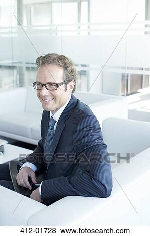 Businessman sitting on sofa in office lobby View Large Photo Image Stock Photo - Businessman sitting on sofa in office lobby. Fotosearch