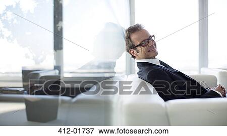 Businessman sitting on sofa in office lobby View Large Photo Image Stock Photo - Businessman sitting on sofa in office lobby. Fotosearch