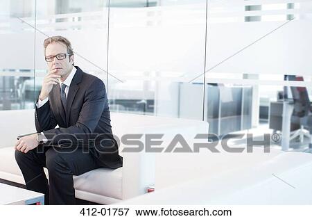 Stock Photo - Businessman sitting on sofa in office lobby. Fotosearch