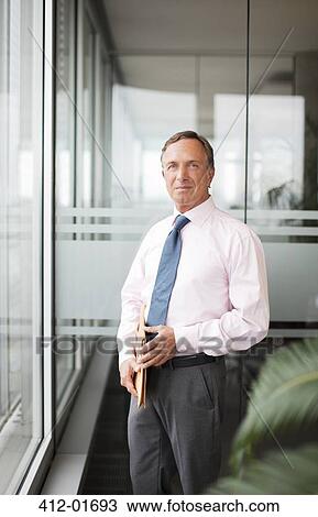 Businessman standing at office window View Large Photo Image Stock Image - Businessman standing at office window. Fotosearch