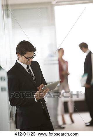 Businessman using digital tablet in office hallway View Large Photo Image Stock Image - Businessman using digital tablet in office hallway. Fotosearch
