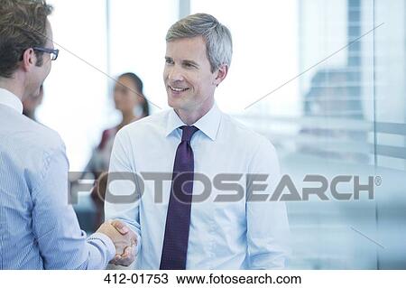 Stock Image - Businessmen shaking hands in office. Fotosearch