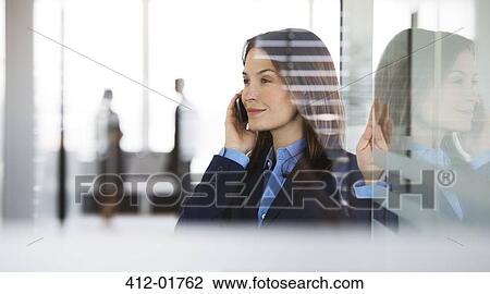 Stock Image - Businesswoman talking on cell phone in office. Fotosearch