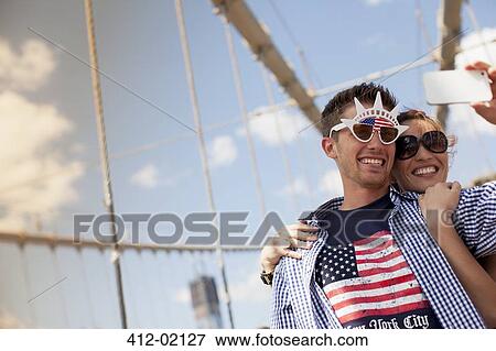 Stock Photo - Couple in novelty sunglasses taking picture on urban bridge. Fotosearch