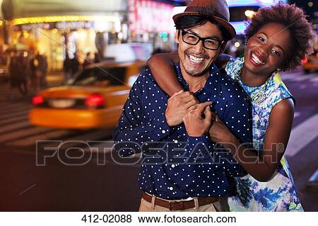 Stock Photo - Couple smiling on city street at night. Fotosearch