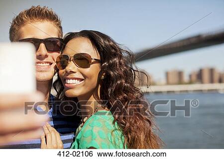 Stock Photograph - Couple taking picture of themselves by urban bridge. Fotosearch