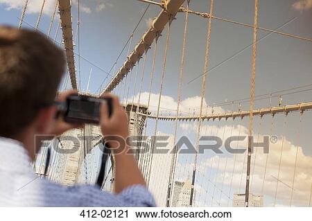 Stock Image - Man taking picture of urban bridge. Fotosearch