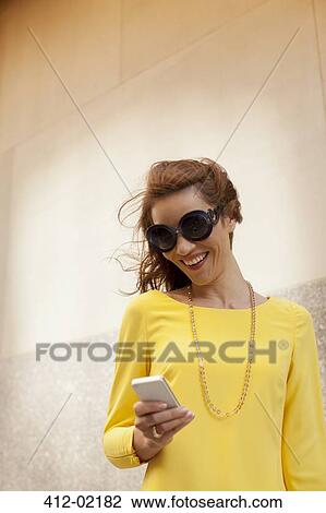 Stock Image - Woman using cell phone on city street. Fotosearch