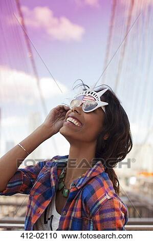 Stock Image - Woman wearing novelty sunglasses outdoors. Fotosearch