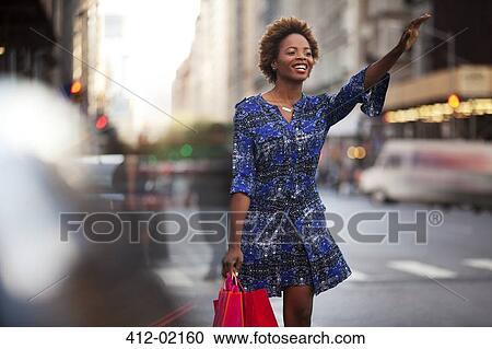 Stock Image - Woman with shopping bags hailing taxi on city street. Fotosearch