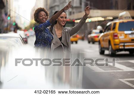 Stock Photography - Women hailing taxi on city street. Fotosearch
