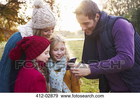Stock Photo - Family using cell phone together outdoors. Fotosearch