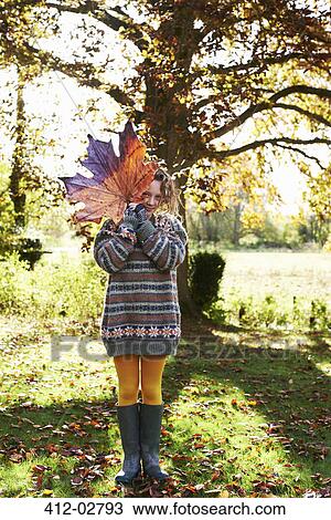 Stock Image - Girl playing with autumn leaf outdoors. Fotosearch