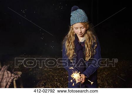 Stock Image - Girl playing with sparkler outdoors. Fotosearch