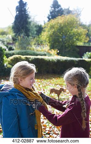 Stock Photo - Girl tying sister's scarf outdoors. Fotosearch