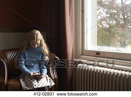 Stock Image - Girl using digital tablet in armchair. Fotosearch