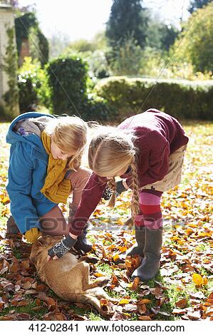Stock Image - Girls petting dog in autumn leaves. Fotosearch