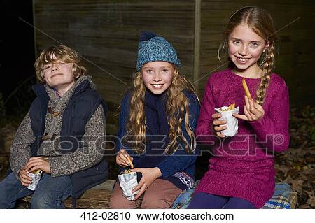 Stock Image - Smiling children eating french fries at night. Fotosearch
