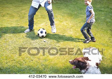 Stock Image - Boy playing soccer with dog outdoors. Fotosearch