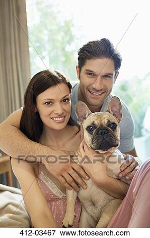 Stock Photo - Couple hugging dog on bed. Fotosearch