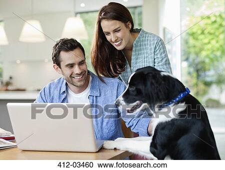 Stock Image - Couple petting dog at table. Fotosearch