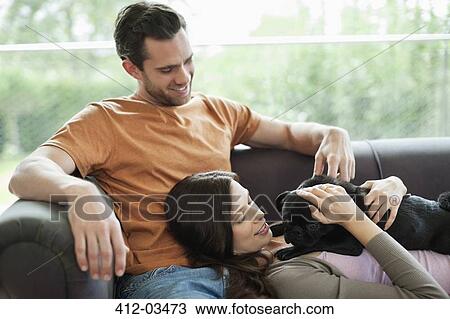 Stock Image - Couple relaxing with dog on sofa. Fotosearch