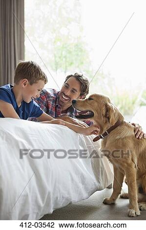Stock Image - Father and son petting dog in bedroom. Fotosearch