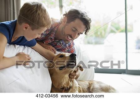 Stock Photograph - Father and son petting dog on sofa. Fotosearch