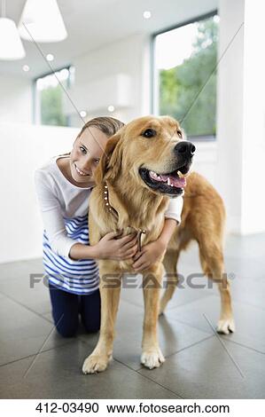 Stock Image - Girl hugging dog indoors. Fotosearch