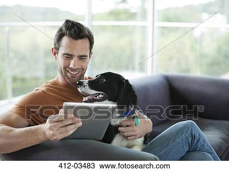 Stock Image - Man petting dog and using tablet computer. Fotosearch