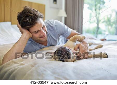 Stock Photo - Man petting dog on bed. Fotosearch