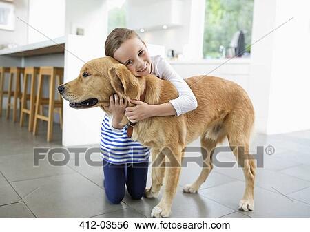 Stock Photograph - Smiling girl hugging dog in kitchen. Fotosearch