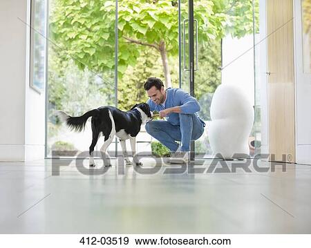 Stock Photo - Smiling man petting dog in kitchen. Fotosearch